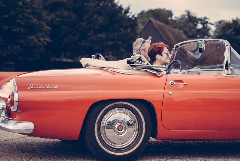 Older couple driving orange thunderbird