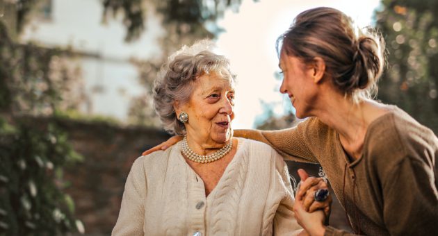 An elderly lady and a younger woman smiling at one another.